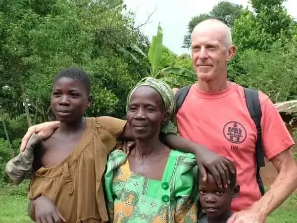 An older male IVI volunteer smiling while posing outdoors with an elderly woman and two children from a local community.