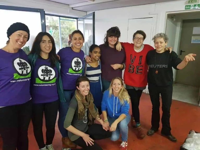 A diverse group of ten IVI volunteers smiling and posing together indoors after a successful project, with some wearing purple IVI t-shirts.